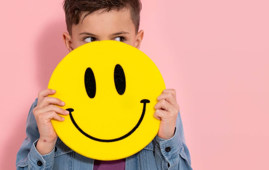 Afbeelding waarop een jongetje zich verschuild achter een smiley emoji.