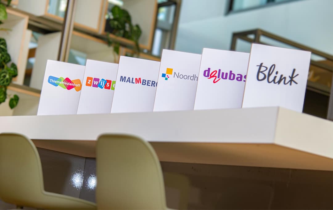 Op de afbeelding zie je bordjes met namen van de uitgeverijen blink, delubas, noordhoff, malmberg, zwijsen en thieme meullenhoff.
