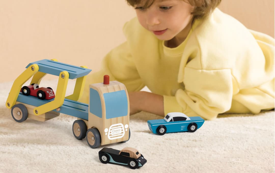 Op de afbeelding zie je een jongetje dat speelt met houten voertuigen.
