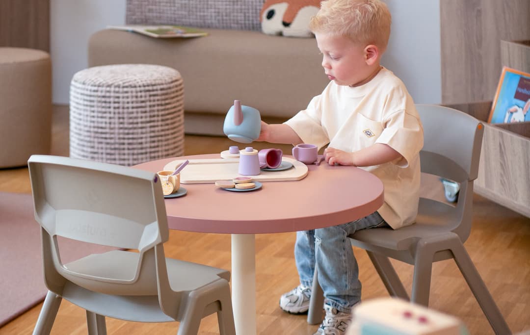 Jongetje zit aan tafel met een tablet met speel kopjes en bestek
