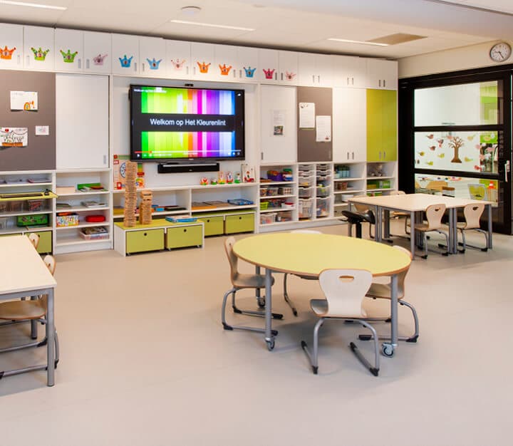 Op de afbeelding zie je een klaslokaal met kastjes en een digibord