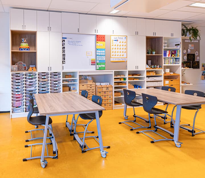 Op de afbeelding zie je tafels en stoelen met een kastenwand op de achtergrond.