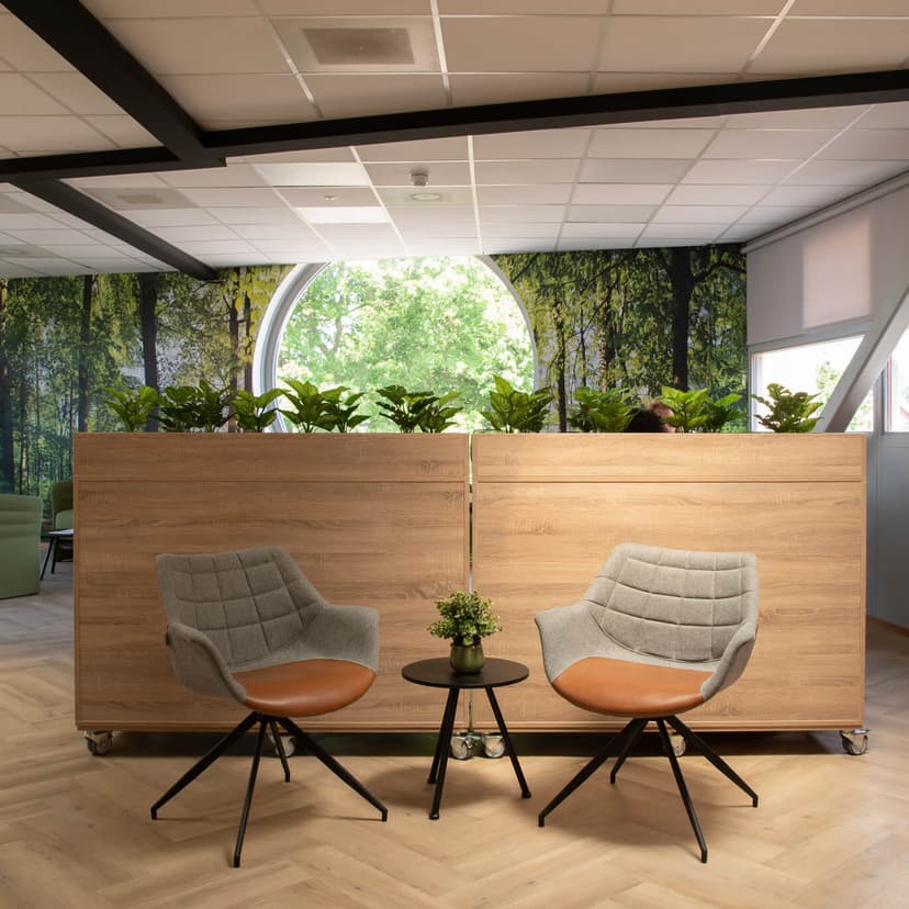 Op de afbeelding zie je bosbehang en daarvoor staan groene luxe stoelen.