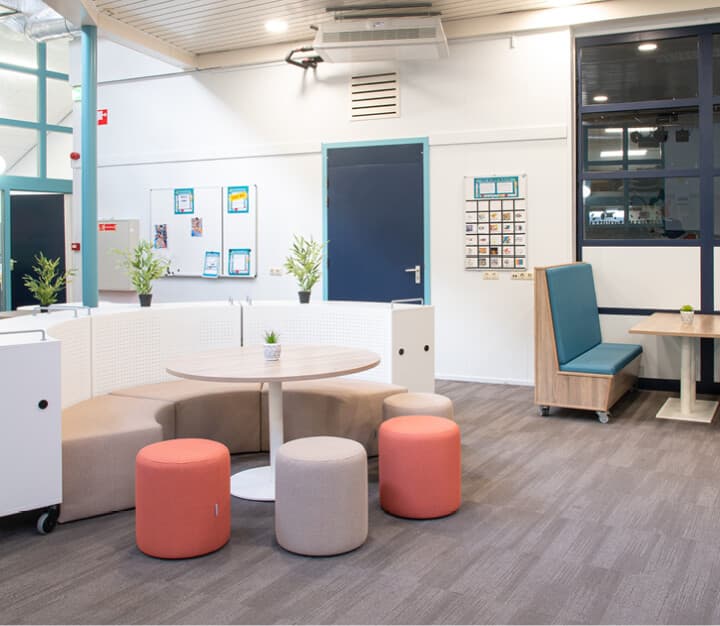 Op de afbeelding zie je aula ingericht met blauw, oranje en wit meubilair.