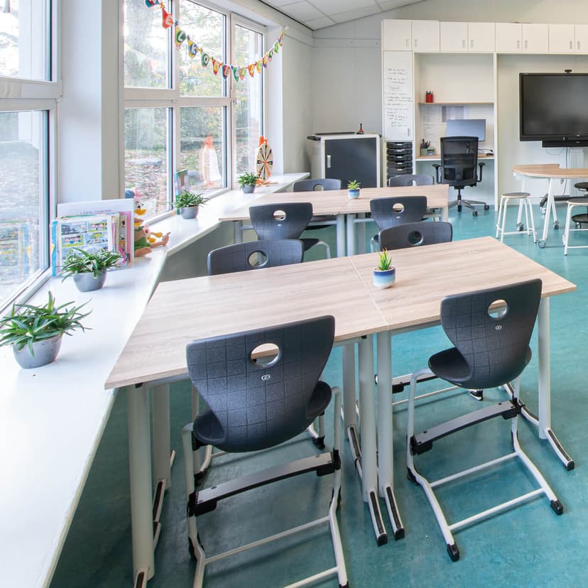 Op de afbeelding zie je een klaslokaal met blauwe vloer, ronde tafel en poefjes.