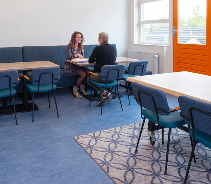 Op de afbeelding zie je een klaslokaal met verschillende tafels en een werkhuisje.