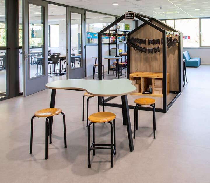 Op de afbeelding zie je een klaslokaal met banken met opbergbakken en wolkentafels.