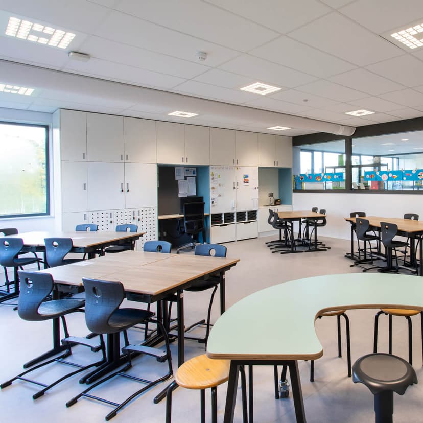 Je ziet op de afbeelding een klaslokaal met uitlegtafel en groepstafels.